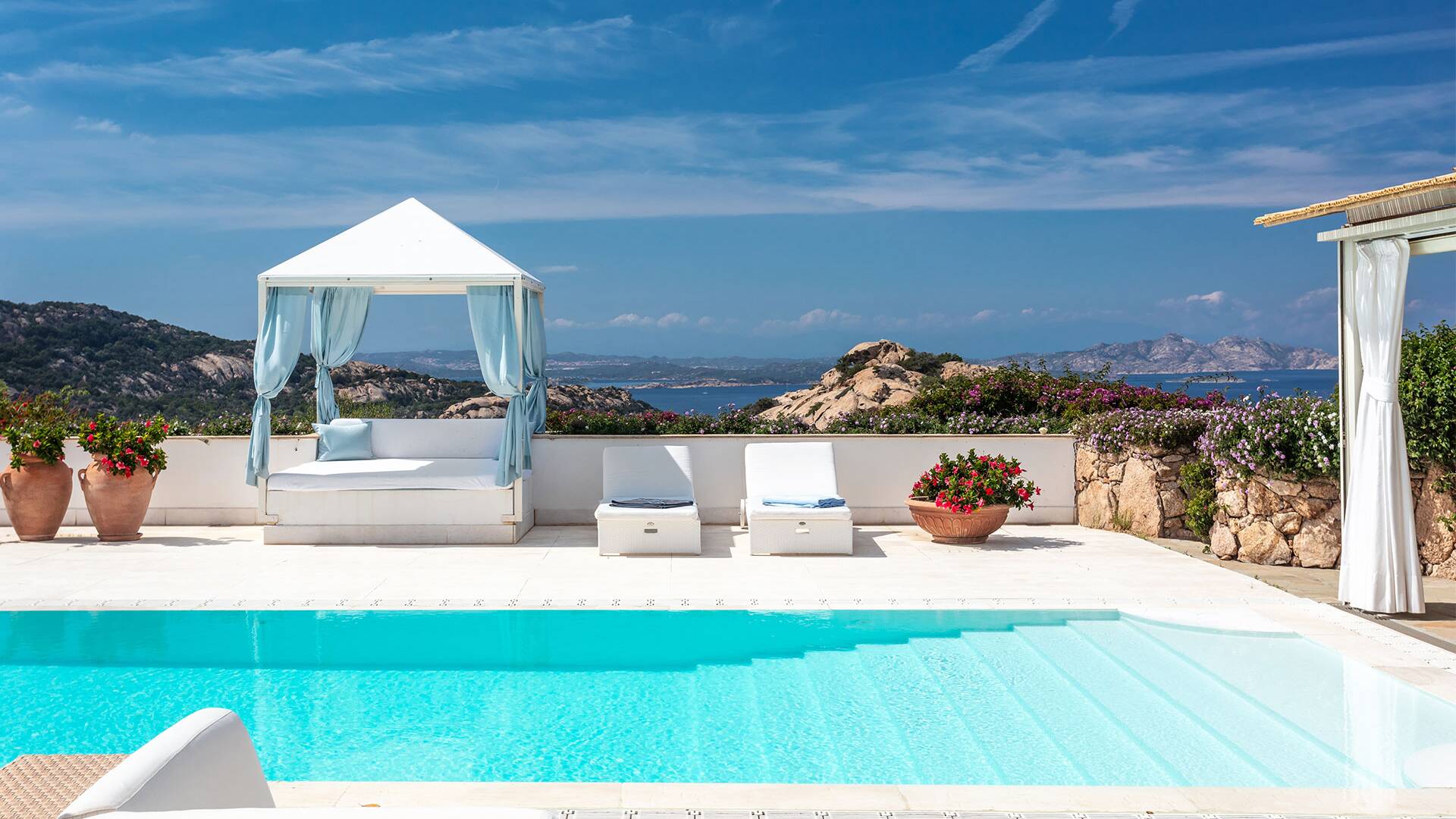 infinity swimming pool with covered sunbeds and sea view